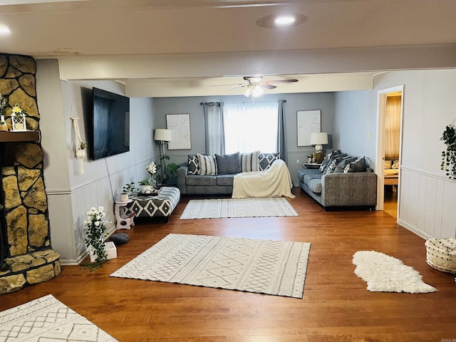 living room featuring a wainscoted wall, ceiling fan, a fireplace, and wood finished floors