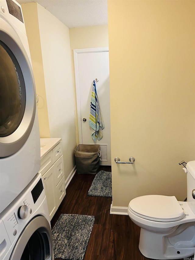 interior space with toilet, stacked washing maching and dryer, baseboards, and wood finished floors