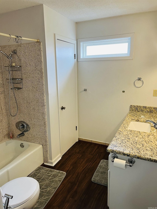 bathroom with a textured ceiling, toilet, wood finished floors, baseboards, and washtub / shower combination