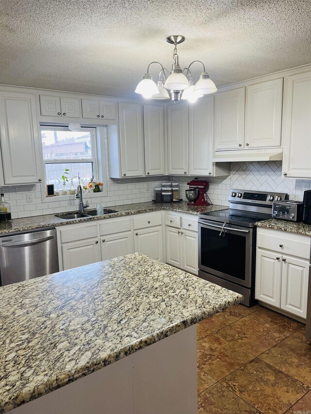 kitchen with light stone counters, stainless steel appliances, white cabinets, a sink, and under cabinet range hood