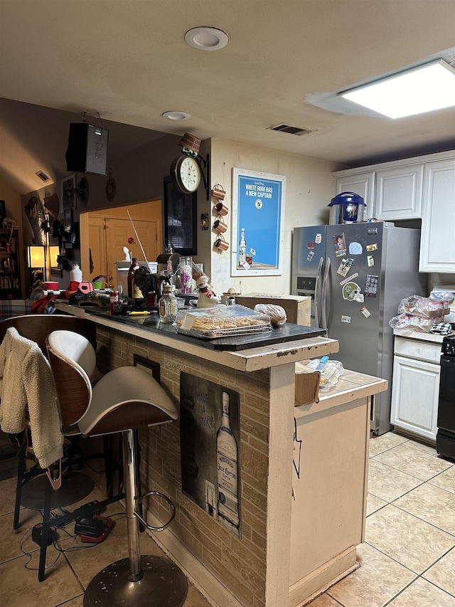 kitchen with a breakfast bar area, stainless steel fridge, kitchen peninsula, and white cabinets