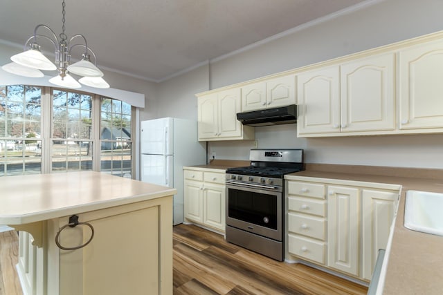 kitchen with pendant lighting, white refrigerator, stainless steel gas range oven, light wood-type flooring, and crown molding