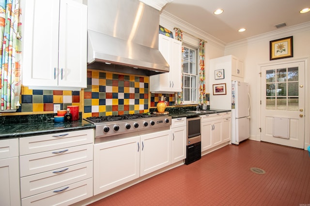 kitchen with extractor fan, white refrigerator, stainless steel gas stovetop, decorative backsplash, and white cabinetry