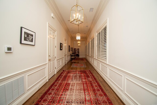 hallway with dark hardwood / wood-style flooring, ornamental molding, and an inviting chandelier