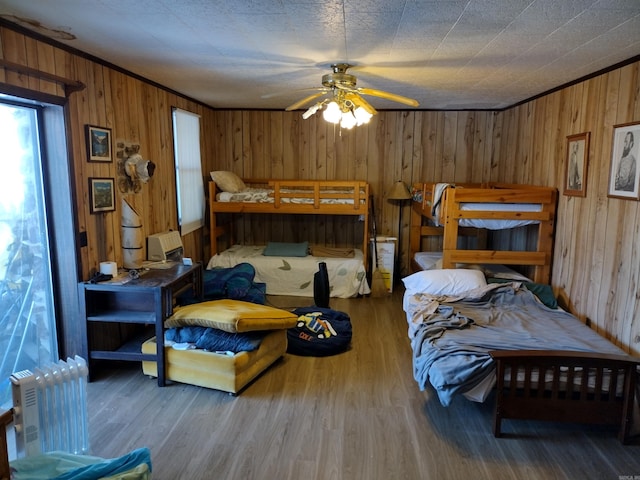 bedroom with dark wood-type flooring, ceiling fan, wood walls, radiator, and ornamental molding