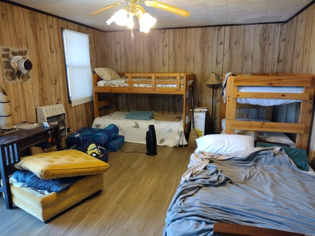 bedroom with ceiling fan, wood walls, and light wood-type flooring