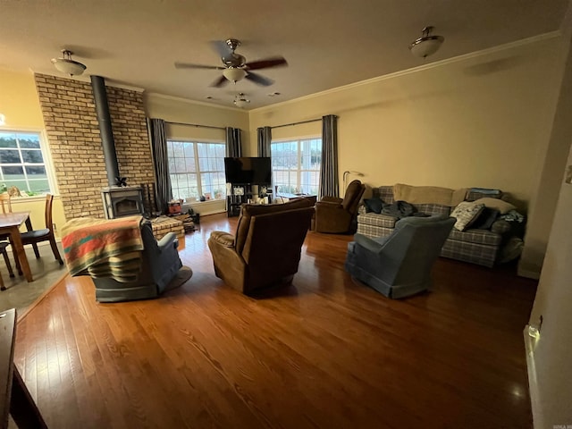 living room with a wood stove, ceiling fan, brick wall, crown molding, and dark hardwood / wood-style floors