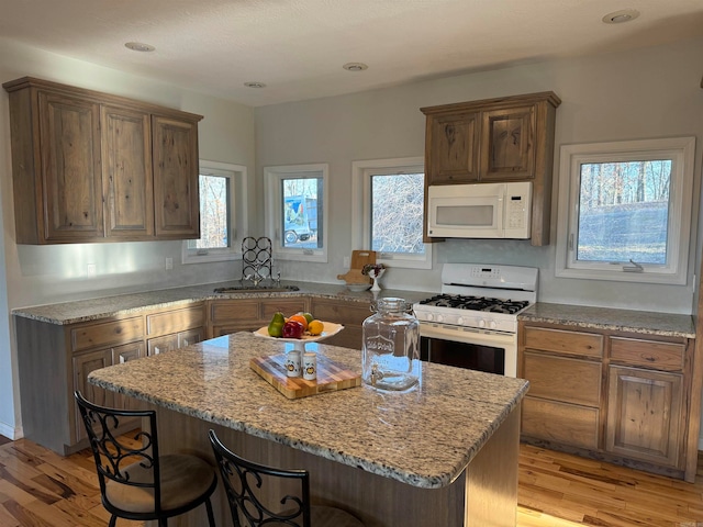 kitchen with a kitchen island, light stone countertops, light hardwood / wood-style flooring, white appliances, and sink