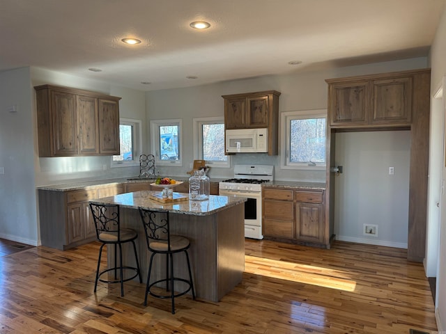 kitchen with white appliances, light stone counters, a kitchen breakfast bar, a center island, and hardwood / wood-style flooring