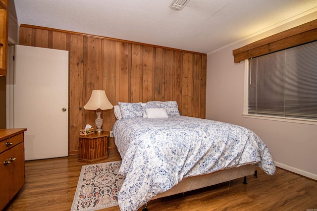 bedroom with wood-type flooring, wooden walls, a textured ceiling, and crown molding