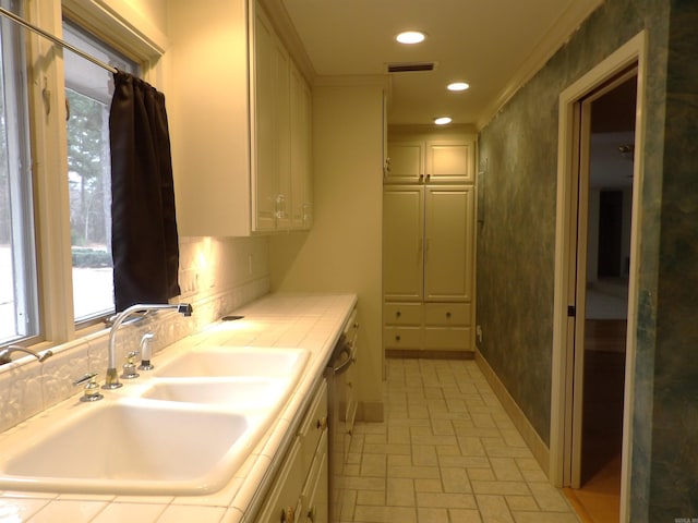 kitchen with white dishwasher, tile counters, crown molding, and sink