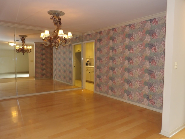 empty room featuring an inviting chandelier, light hardwood / wood-style floors, and crown molding