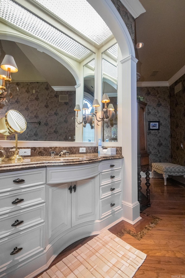 bathroom featuring a chandelier, vanity, wood-type flooring, crown molding, and ornate columns