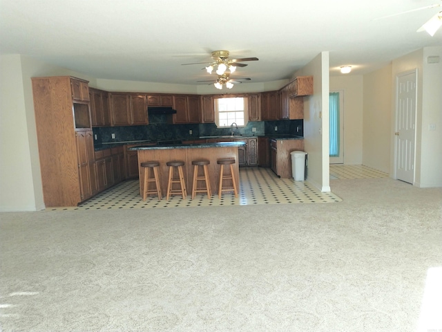 kitchen featuring a breakfast bar, a kitchen island, ceiling fan, and light colored carpet