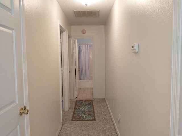 corridor with light carpet and a textured ceiling