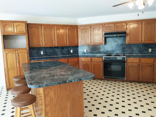 kitchen featuring light tile flooring, a kitchen bar, ceiling fan, tasteful backsplash, and oven