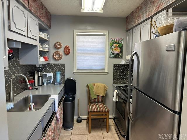 kitchen with light tile patterned flooring, backsplash, electric stove, stainless steel fridge, and sink