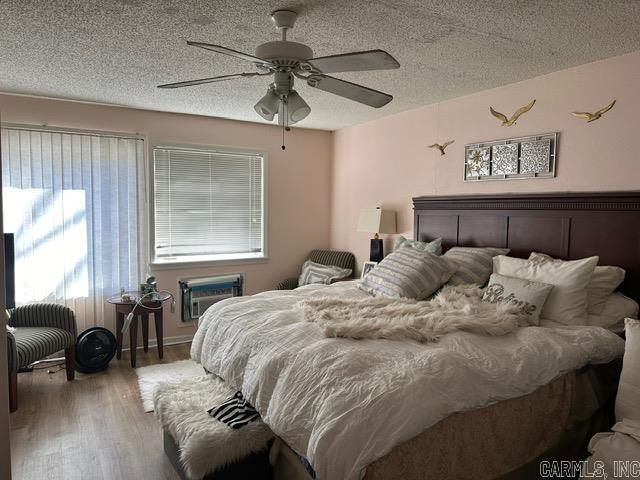 bedroom featuring ceiling fan, multiple windows, a textured ceiling, and hardwood / wood-style flooring