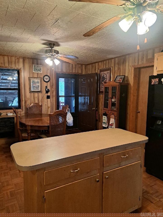 kitchen featuring black fridge, light countertops, wood walls, and ceiling fan