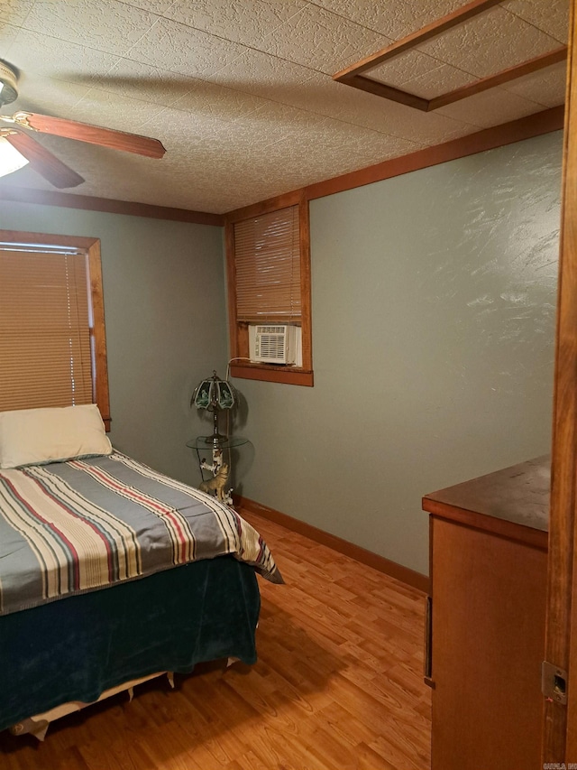 bedroom featuring a textured ceiling, wood finished floors, cooling unit, baseboards, and ceiling fan