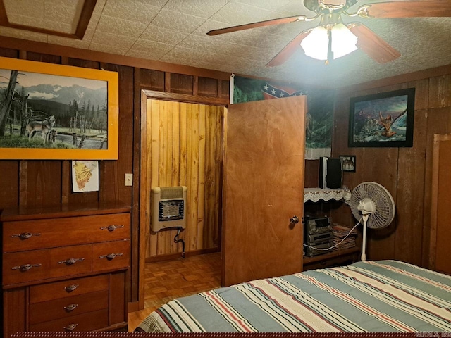 bedroom with heating unit, wooden walls, and ceiling fan