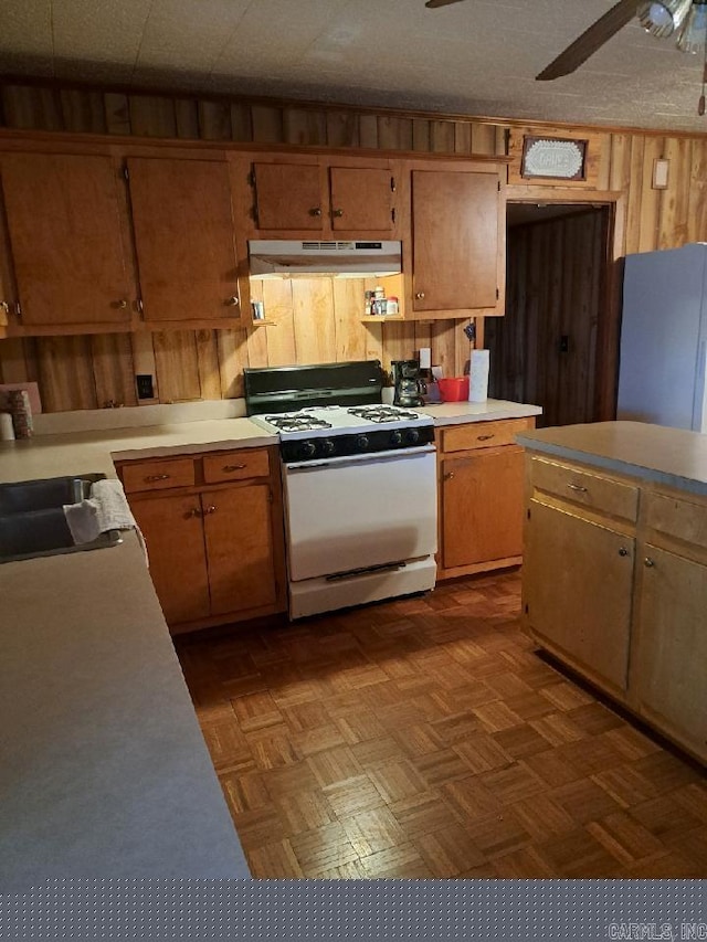 kitchen featuring gas range gas stove, under cabinet range hood, wood walls, light countertops, and freestanding refrigerator