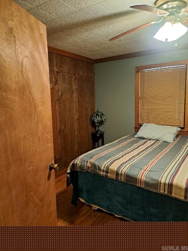 bedroom with a ceiling fan, wood finished floors, and wood walls