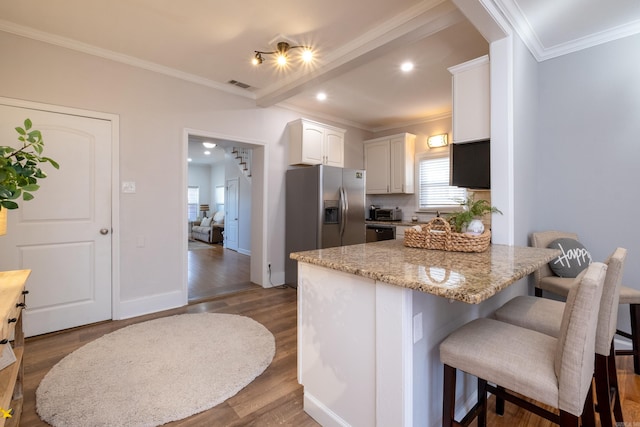 kitchen featuring a breakfast bar, light stone counters, white cabinets, hardwood / wood-style floors, and ornamental molding