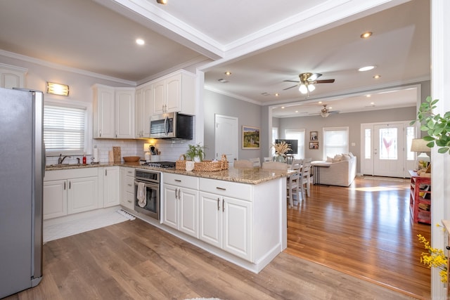 kitchen with light stone counters, ornamental molding, appliances with stainless steel finishes, white cabinetry, and light wood-type flooring