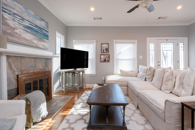 living room featuring ceiling fan, crown molding, a fireplace, and light hardwood / wood-style floors