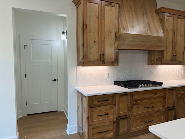 kitchen with light wood-type flooring, stainless steel gas stovetop, custom exhaust hood, and decorative backsplash