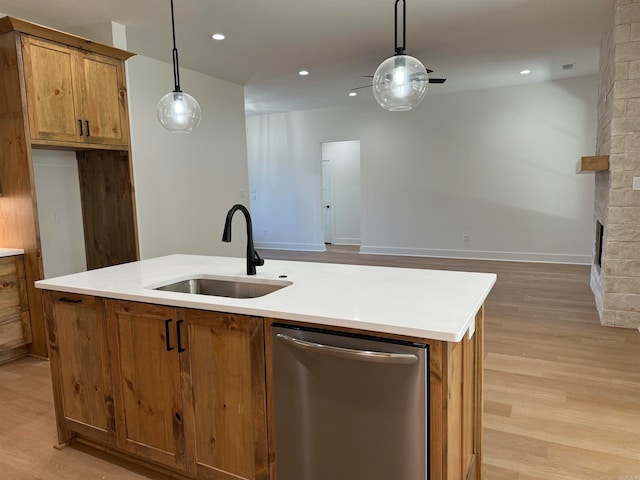 kitchen featuring decorative light fixtures, a center island with sink, stainless steel dishwasher, sink, and light wood-type flooring