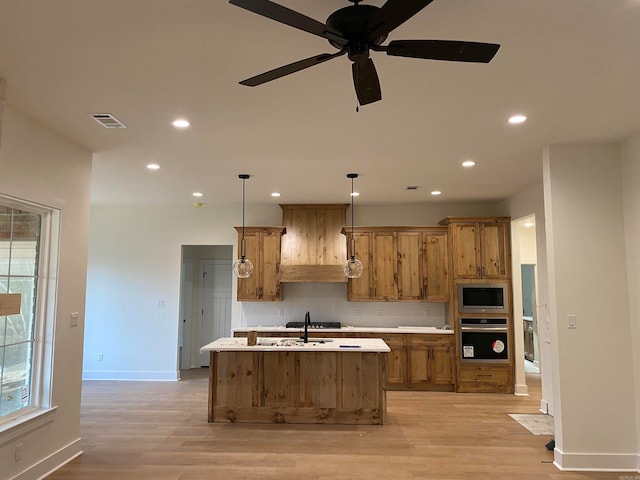 kitchen with an island with sink, hanging light fixtures, ceiling fan, and appliances with stainless steel finishes