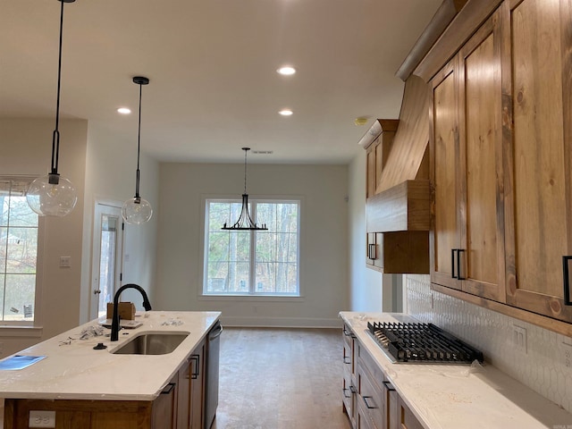 kitchen featuring light stone counters, a chandelier, sink, an island with sink, and pendant lighting