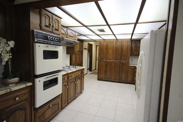 kitchen featuring light tile floors, tasteful backsplash, white appliances, and dark brown cabinets