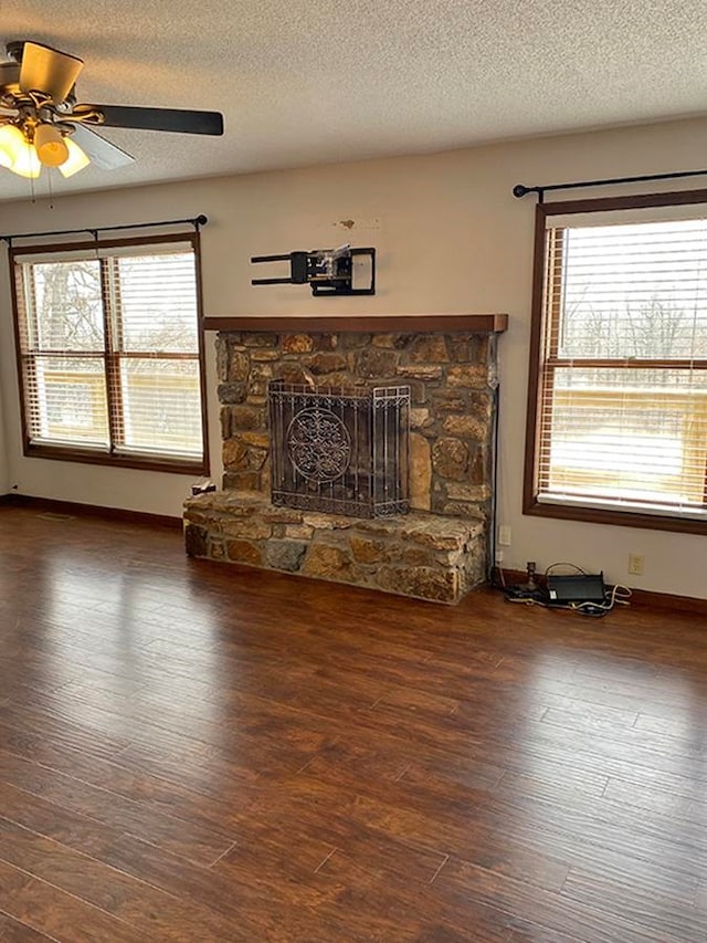 unfurnished living room featuring a wealth of natural light, a fireplace, ceiling fan, and dark hardwood / wood-style flooring