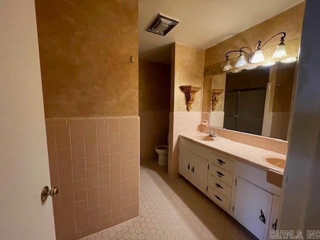 bathroom with tile walls, toilet, dual bowl vanity, tile floors, and tasteful backsplash