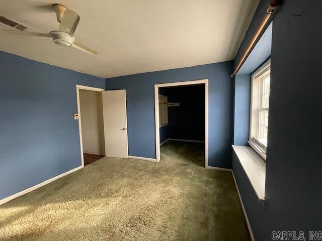 unfurnished bedroom featuring ceiling fan, a closet, dark colored carpet, and a walk in closet