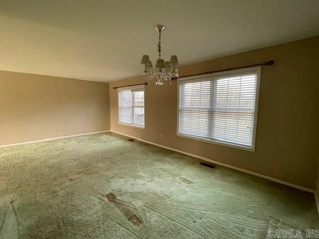 empty room featuring a chandelier and carpet flooring