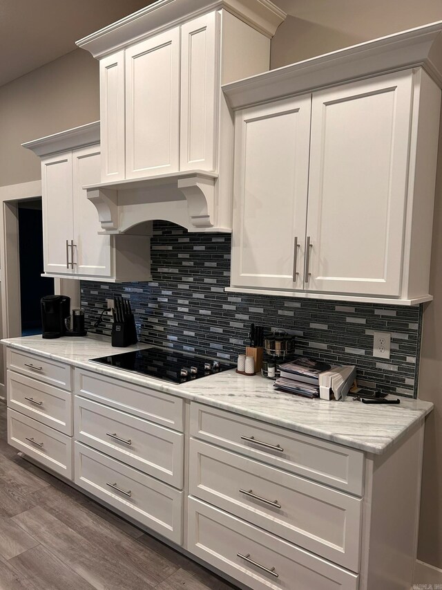 kitchen featuring premium range hood, black electric cooktop, light stone countertops, hardwood / wood-style floors, and white cabinetry