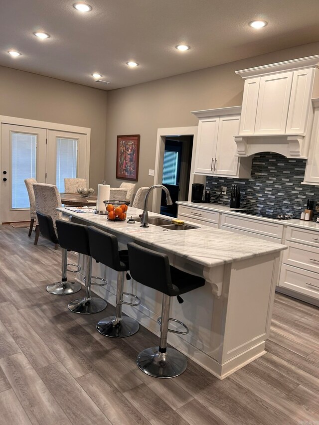 kitchen featuring hardwood / wood-style flooring, white cabinetry, a breakfast bar area, and an island with sink