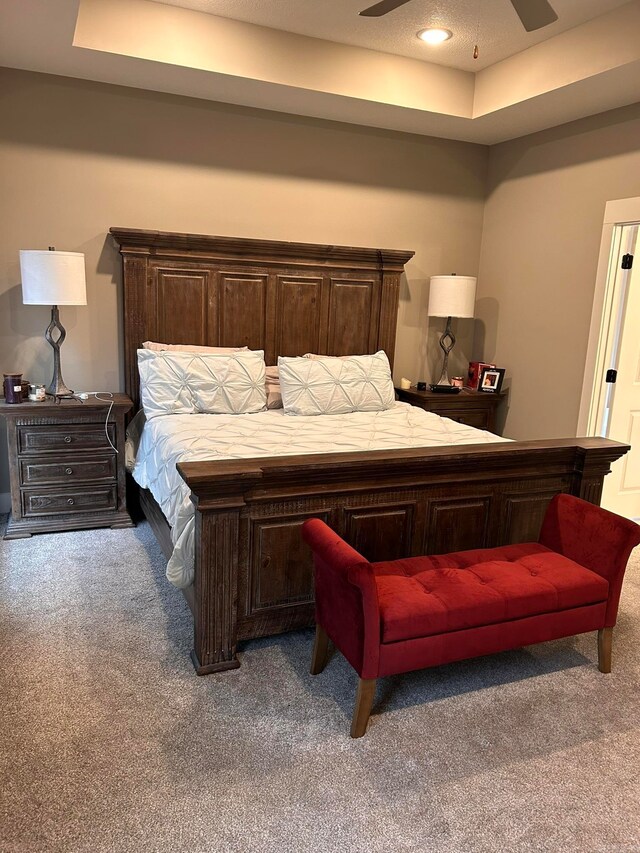 carpeted bedroom with a tray ceiling and ceiling fan