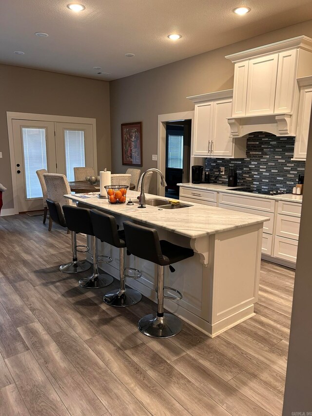 kitchen featuring a kitchen island with sink, sink, white cabinets, light hardwood / wood-style flooring, and black gas stovetop