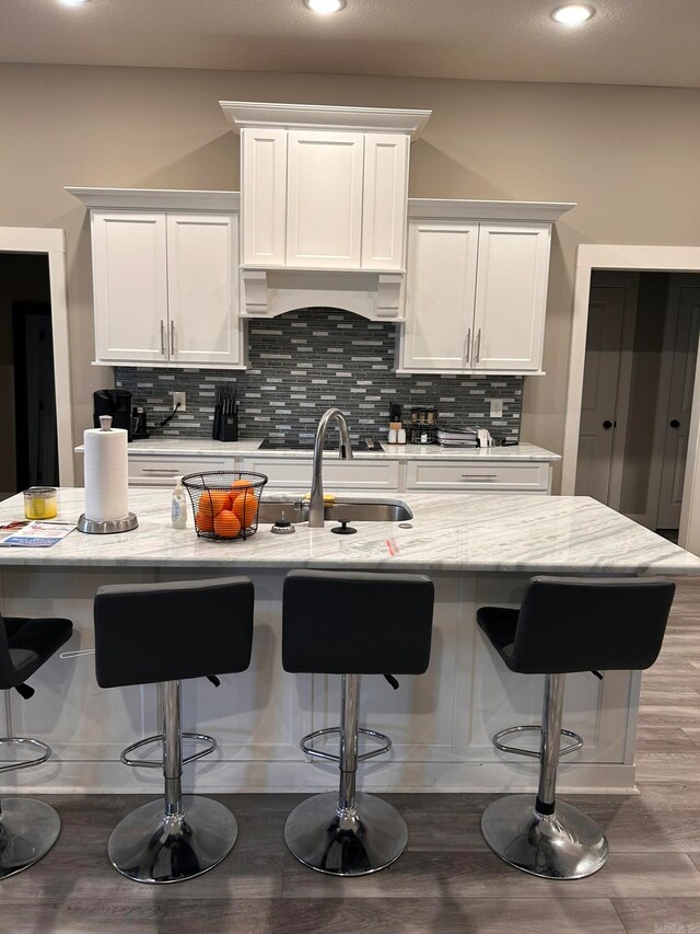 kitchen featuring white cabinetry, a kitchen bar, custom exhaust hood, wood-type flooring, and tasteful backsplash