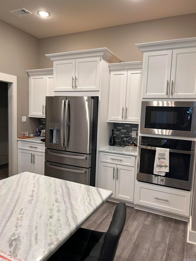 kitchen featuring backsplash, white cabinetry, stainless steel appliances, and hardwood / wood-style floors