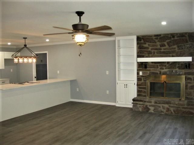 unfurnished living room featuring a stone fireplace, dark hardwood / wood-style floors, ceiling fan, and ornamental molding