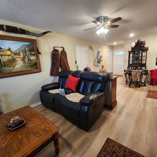 living room with a textured ceiling, ceiling fan, and light wood-type flooring