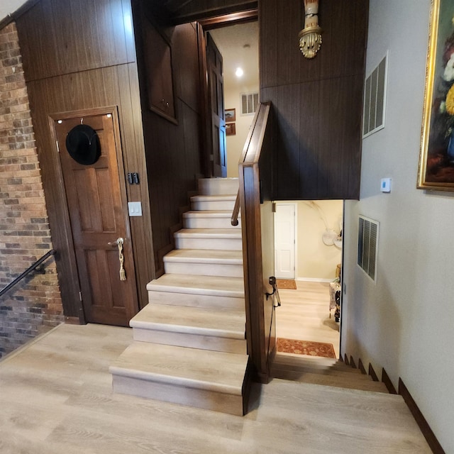 staircase featuring brick wall and light hardwood / wood-style floors