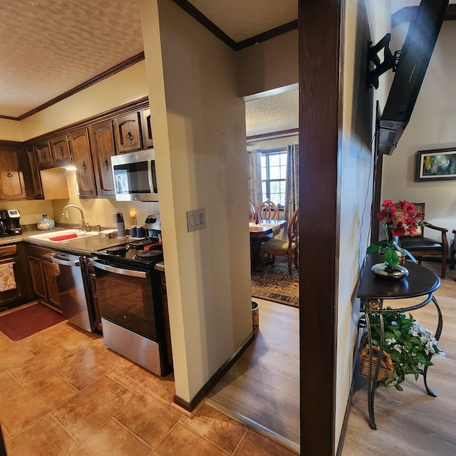 kitchen with ornamental molding, dark brown cabinets, appliances with stainless steel finishes, and sink