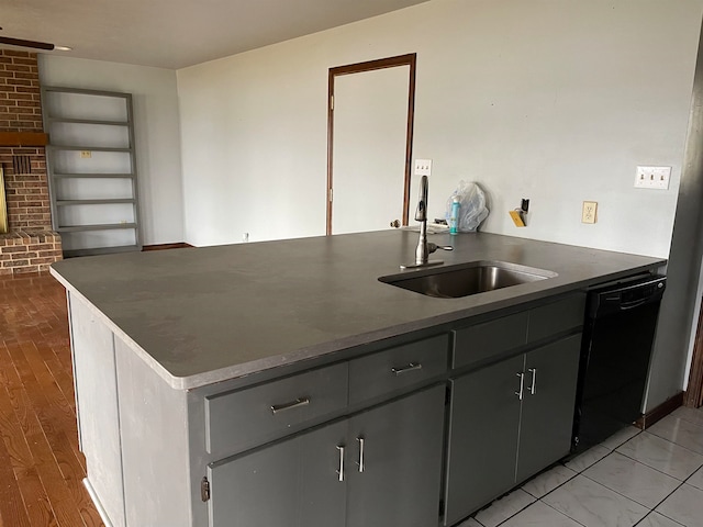 kitchen with sink, a brick fireplace, black dishwasher, gray cabinetry, and light tile floors